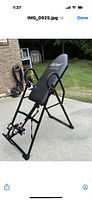 Full view of black Teeter inversion table set up outdoors on concrete surface, showing padded backrest and metal frame.