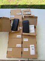 Lot of 14 brown cardboard boxes with several power banks displayed on top, some boxes opened revealing black power banks inside.