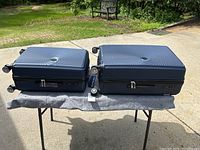 Photo of two matching blue hard shell suitcases placed on a folding table outdoors, showing textured circular ripple design and spinner wheels.