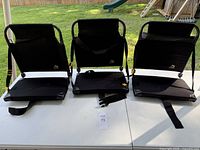 Three black stadium chairs shown from the front on a white table outdoors with green grass background