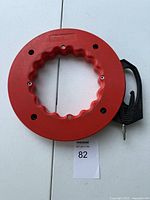 Top view of red steel tape measure with black handle, showing grooved center and screws on the front side.