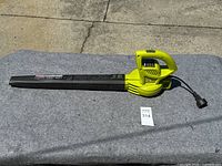 Yellow and black Sun Joe corded electric leaf blower with long black nozzle and power cord displayed on gray surface.