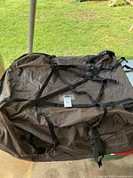 Top view of large brown fabric zippered cargo bag with multiple black adjustable straps and buckles spread out on flat surface outdoors.