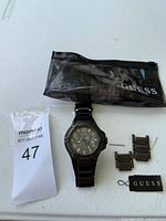 Photo of the Guess black stainless steel watch, extra metal links and pins, and black Guess-branded pouch.