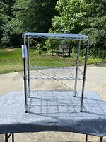 Front view of a metal wire shelving unit with three shelves placed on a grey cloth outdoors.