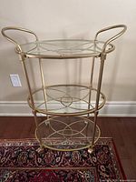 Front view showing three glass tiers, gold frame, casters