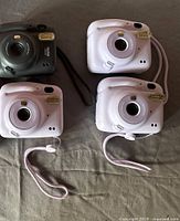 Front view of four Instax Mini 11 cameras showing lens, flash units and wrist straps