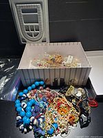 Overall view of box with jewelry inside and pile of necklaces outside