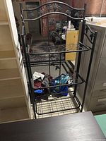 Full view of black metal shelf unit showing leaf motif and three wire shelves