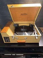 Open suitcase record player showing platter, tonearm, handle, interior branding