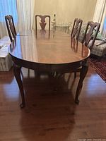 Full view of wooden oval dining table with leaf inserted and cabriole legs