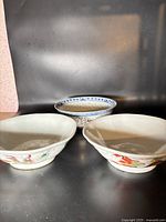Front view showing two bowls with dragon and phoenix painted designs and one bowl with blue and red floral pattern.