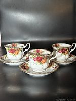 Three sets of bone china teacups and saucers with the Old Country Roses floral pattern and gold trim on a black background.