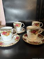 Four bone china coffee cups with matching saucers arranged in pairs, showing floral rose design and gold trim.