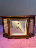Front view of wooden mantel clock with clock face and speaker grilles on each side