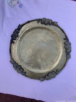 Full view of one brass plate showing grapevine motif around edge and engraved central design