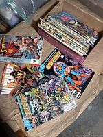 Box filled with numerous comic books, mostly DC Comics titles, including visible 'Crisis', 'The Brave and The Bold', and 'Superman' comics.