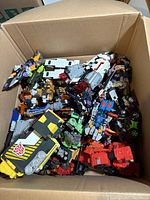 Top view of an open cardboard box filled with multiple Transformers toys and action figures.