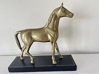 Front-left angled view of the brass horse figurine on a black base showing detailed mane and tail.