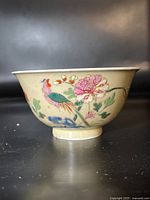 Side view of bowl showing colorful bird and flower painted on cream exterior.