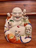 Front view of the porcelain statue showing the laughing Buddha figure with children surrounding him, colorful and detailed with floral patterns.