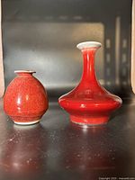 Front view of two Chinese red vases of different shapes showing glossy finishes and color variations.