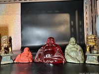 All five figurines arranged side by side on black background: three Buddha statues and two brass Foo Dog statues.