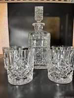 Full set displaying the decanter with stopper surrounded by four matching tumblers, showing the intricate cut glass patterns.