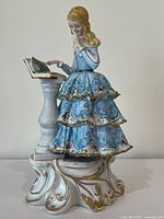 Front view of the porcelain figurine showing the girl reading and detailed dress with gold accents.