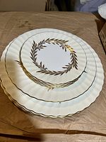 Stack of 3 Minton bone china plates showing varying sizes and gold leaf wreath decoration with scalloped edges.
