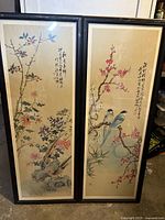 Full view of two framed Chinese art wall hangings showing floral and bird motifs with calligraphy