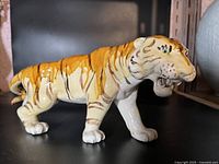Side view of a glazed porcelain tiger figurine on a black surface, showing its orange and brown striped body and detailed face.