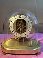 Front view of the vintage German anniversary clock showing the white dial with black numbers under a glass dome and brass base.