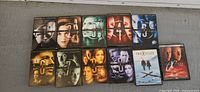 Photo showing all eleven DVD box sets from The X-Files including Seasons 1-9 plus 2 movies, aligned in 2 rows on a gray surface.