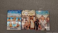 Photo of three DVD box sets of 90210 Seasons 1, 2, and 3 laid side by side on a flat surface.
