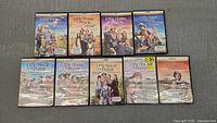 Photo shows nine DVD box sets of Little House On The Prairie seasons 1 through 9, displayed on a gray surface. All cases are intact, season 8 still sealed in plastic.