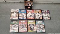 Overview of all nine UFC DVDs displayed in two rows on a gray surface, showing covers and slip box for the first four discs.