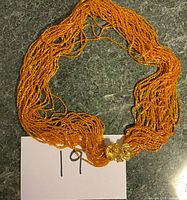 Full view of the amber tone multi-strand beaded necklace laid flat showing the length and color against a dark surface.