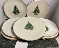 Set of 10 white luncheon plates arranged with visible Christmas tree design and gold rim