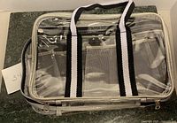 Clear plastic compartmental case closed showing black and white handles and transparent top.