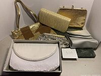 View of six different ladies clutches including various metallic, satin, sequin, and pleated materials.