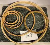Photo showing nine vintage wooden sewing and embroidery hoops in various sizes placed on a marble-like surface with lot number 127 card.