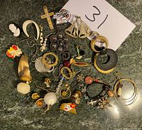 Top view of various mismatched costume jewelry pieces spread out on a dark green marble surface including brooches, earrings, pins, and pendants.
