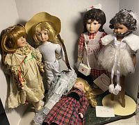 Six porcelain dolls displayed with detailed clothing and accessories, two lying down and four standing on bases