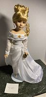 Full standing view of the porcelain doll dressed in a flowing white satin gown with floral bead accents, showing overall condition and height.