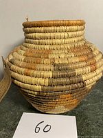 Close-up of a handmade woven reed basket showing the texture and color variations of natural reed material with a rounded body and narrow neck