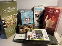 Photo showing a collection of boxes including photo display, photo box, smartphone sanitizer, floating candle, and other items, arranged on a black surface.