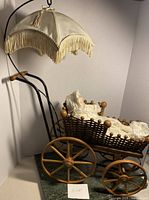 Full view of vintage doll carriage with cream fringed canopy and wooden spoked wheels.