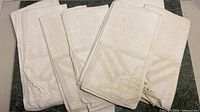 Stack of 8 cream-colored embroidered dinner napkins with scalloped edges visible