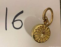 Front view of vintage gold-tone retractable clip-on badge holder showing sunburst decorative design.